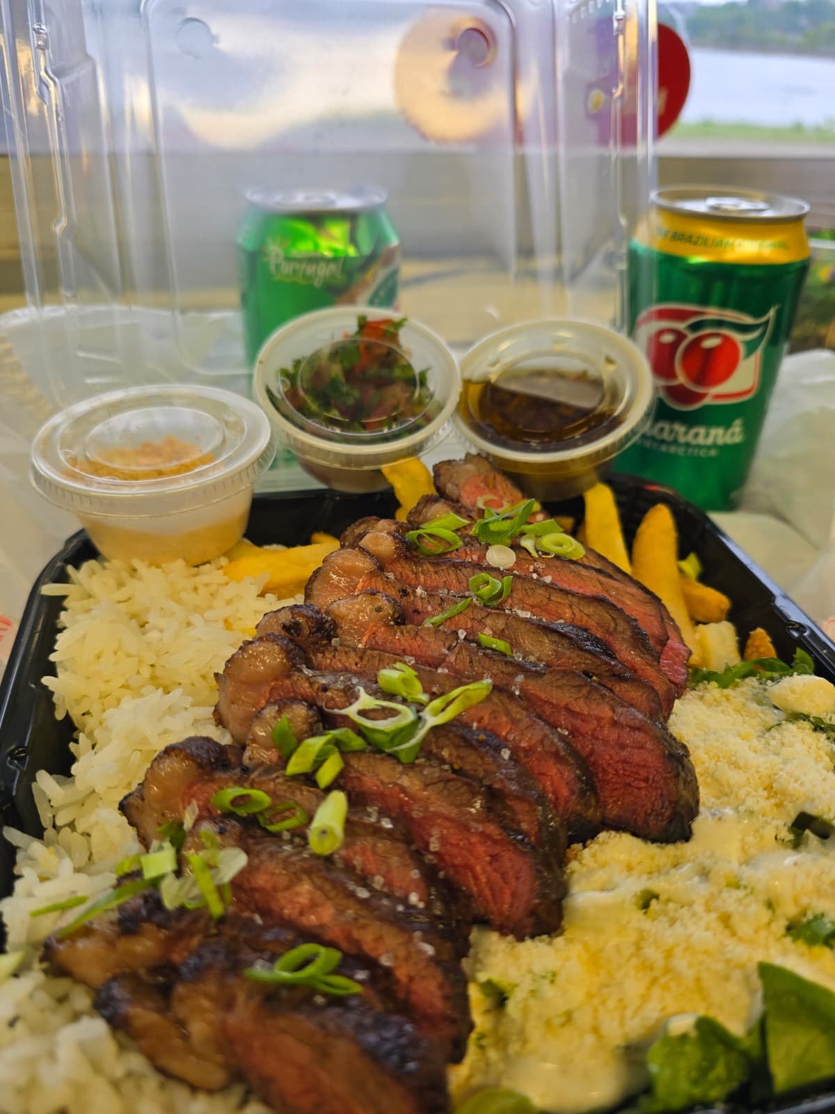 Takeaway grilled steak plate with rice, farofa, sauces, and Guaraná